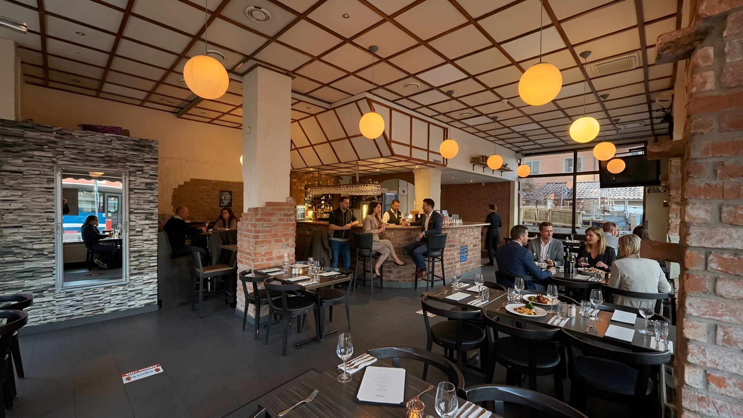 Matsalen och baren inne på Basic Bar Kök i Solna med dukade bord och varm belysning